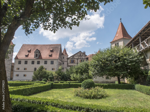 Landscape view of a portion of Harburg Castle. Tree in the foreground with garden and hedges  clear sky with some clouds.