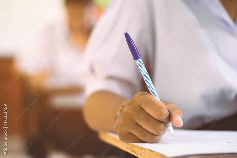 Closeup to hand of student holding pen and taking exam in classroom with stress for education test . Closeup to hand of student holding pen and taking exam in classroom with stress for education test .