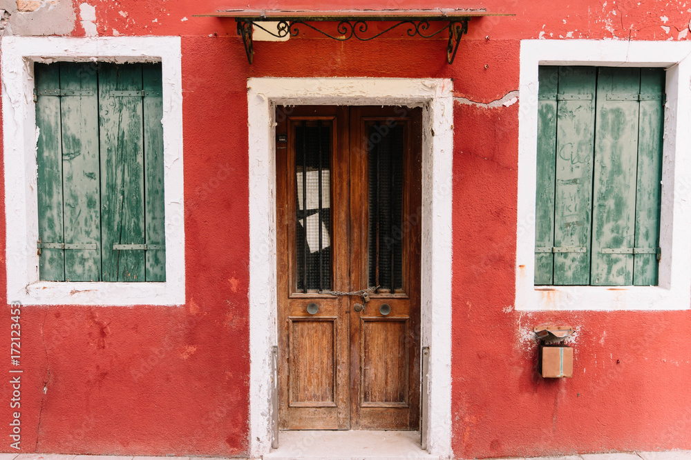 Beautiful colorful house facade on Burano island, north Italy. Red wall with an old wooden door and two windows