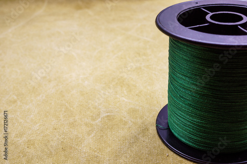 Spool of cord on the background of tarpaulin. Green fishing line. Spool of braided fishing line photo