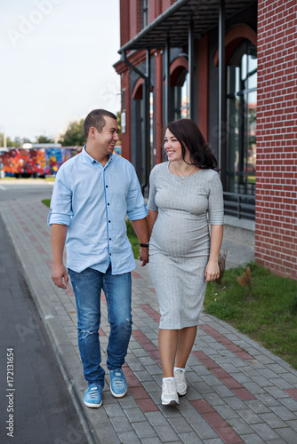family couple men and a young pregnant woman walking holding hands and laughing along the city windows