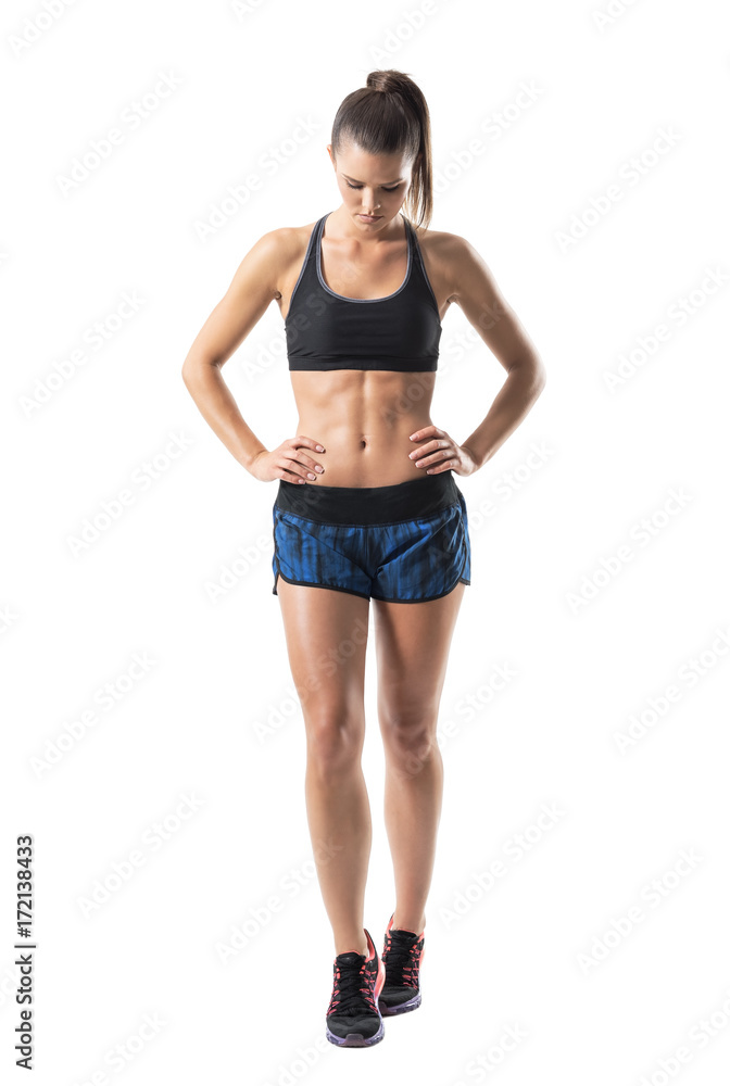 Determined focused fitness woman with hands on hips looking down. Full body length portrait isolated on white studio background. Determined focused fitness woman with hands on hips looking down. Full body length portrait isolated on white studio background.