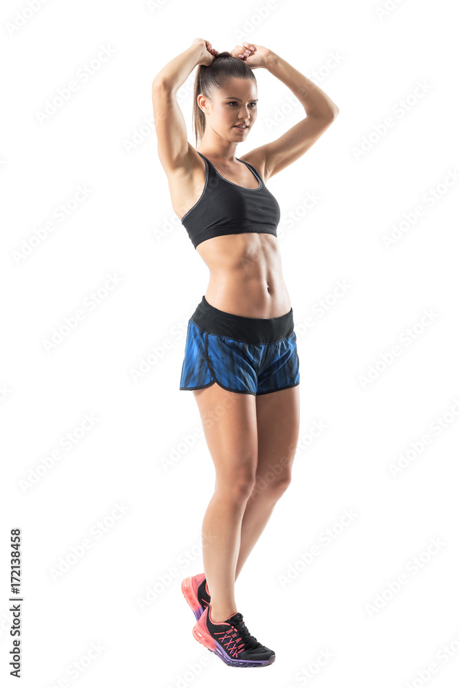 Side view of confident athletic woman adjusting hair in workout  preparation. Full body length portrait isolated on white studio background.  Stock Photo