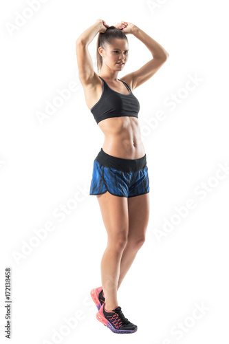 Side view of confident athletic woman adjusting hair in workout preparation. Full body length portrait isolated on white studio background. 