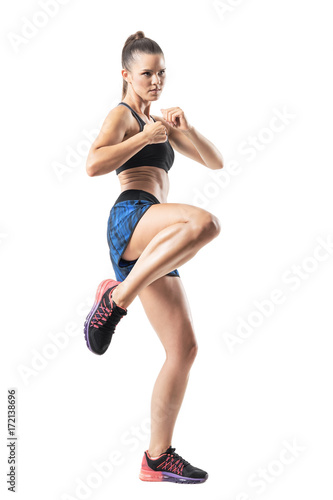 Focused female mma fighter kicking with leg. Stopped action motion. Full body length portrait isolated on white studio background. 