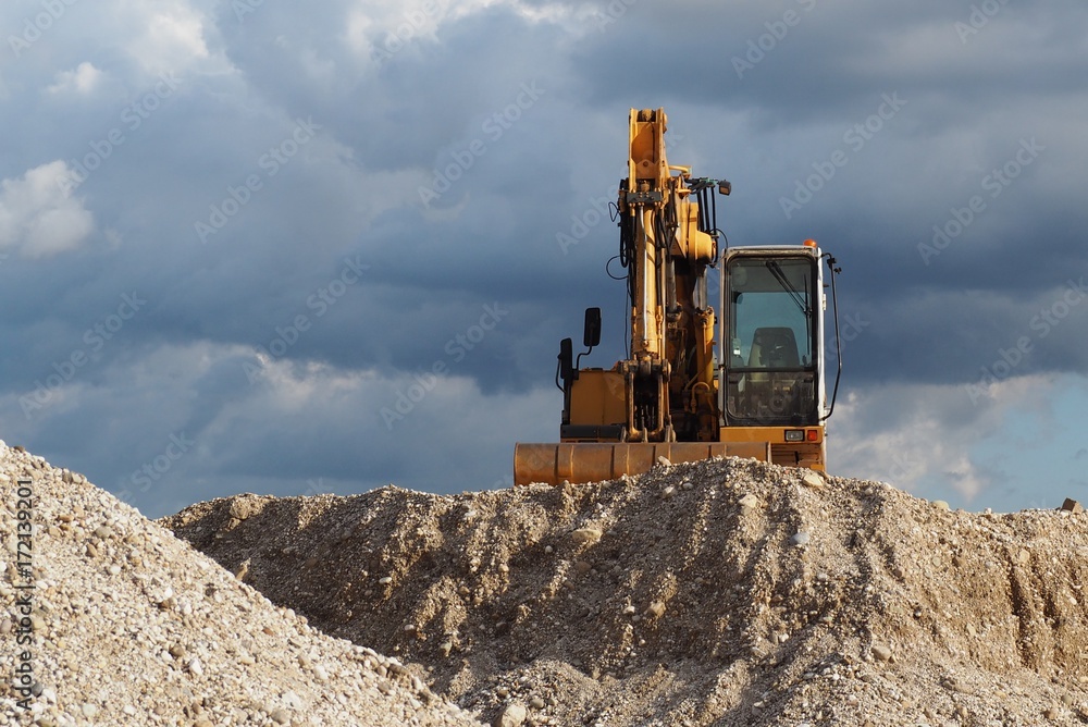 Obraz premium A digger on top of a gravel dune under a cloudy sky