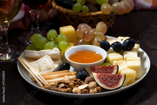 plate of cheeses, snacks and wine on a dark background