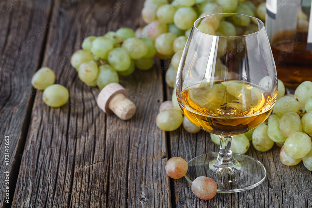 Glass of brandy with brush of grapes on table, harvest holiday Glass of brandy with brush of grapes on table, harvest holiday