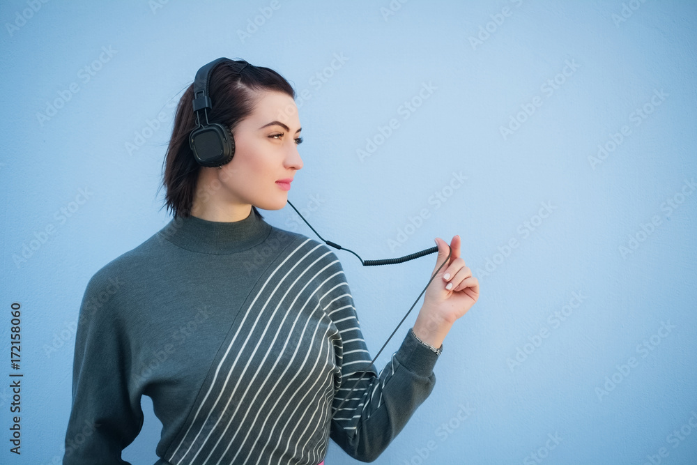 beautiful woman in headphones on blue wall background in gray dress beautiful woman in headphones on blue wall background in gray dress
