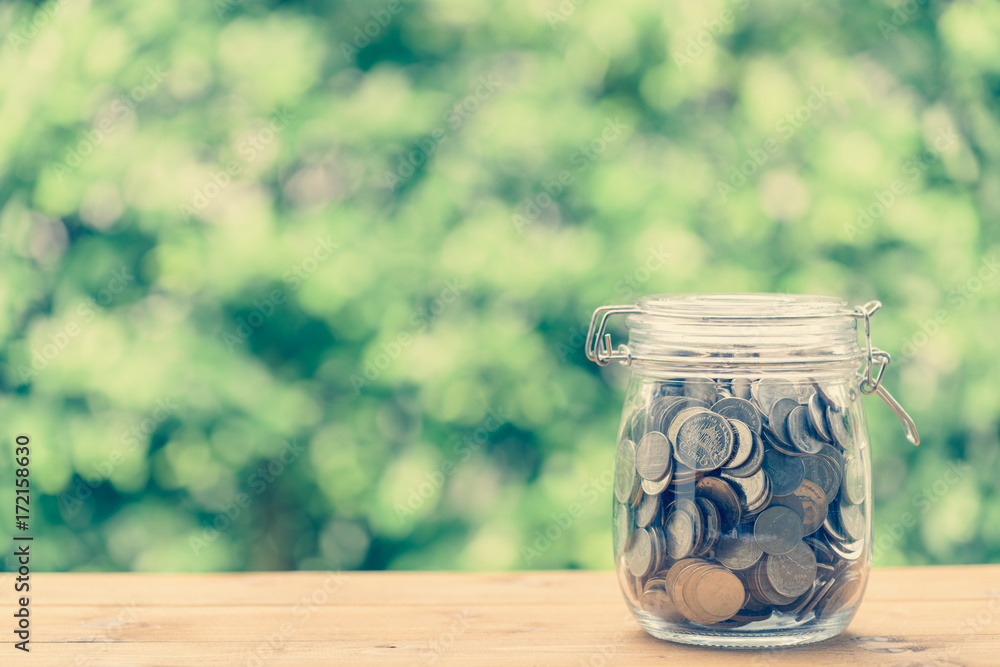 Saving money concept,coins in glass jar on wood table with green nature blurred background Saving money concept,coins in glass jar on wood table with green nature blurred background