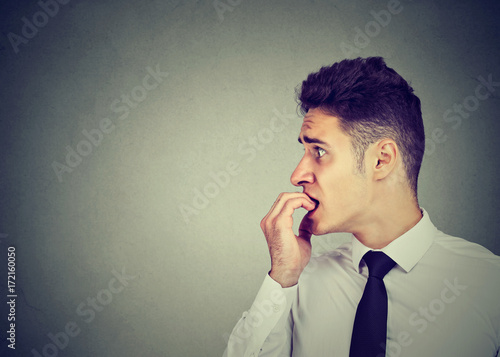 Preoccupied anxious man biting his fingernails looking to the side photo