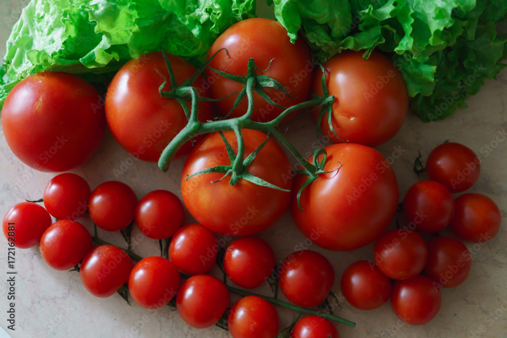 Large and small red tomatoes along with lettuce leaves.