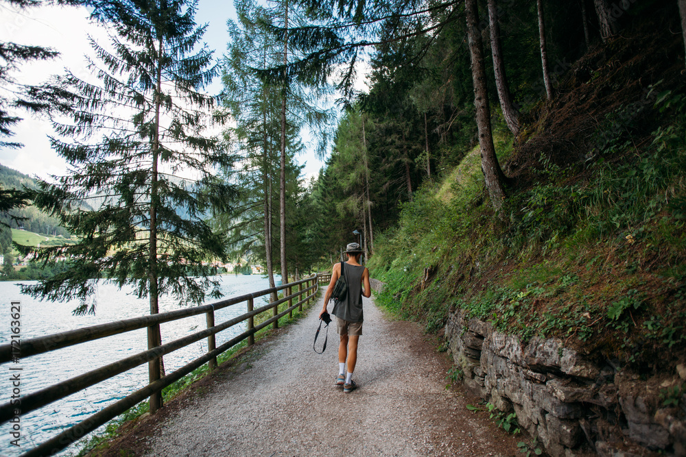 Obraz premium Handsome attractive skinny fit man explores forest trail next to river or lake, walks with photography camera, enjoys outdoors nature, fresh air and forest