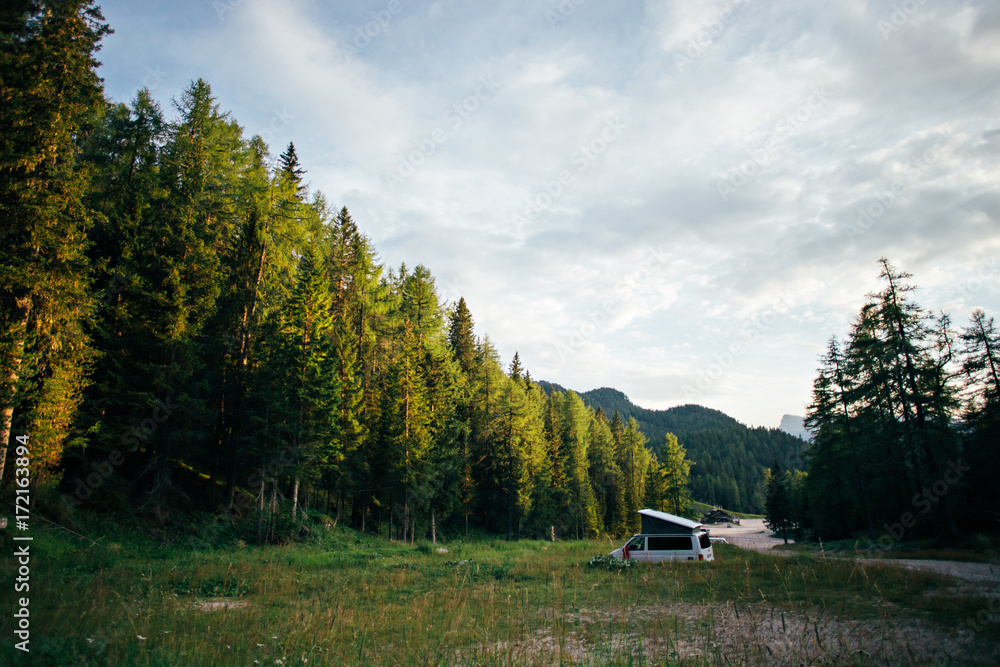 Empty wild camping site lost in green forest on early morning or sunset, with white travel van camped out with folding roof, concept nomad life off grid, adventures