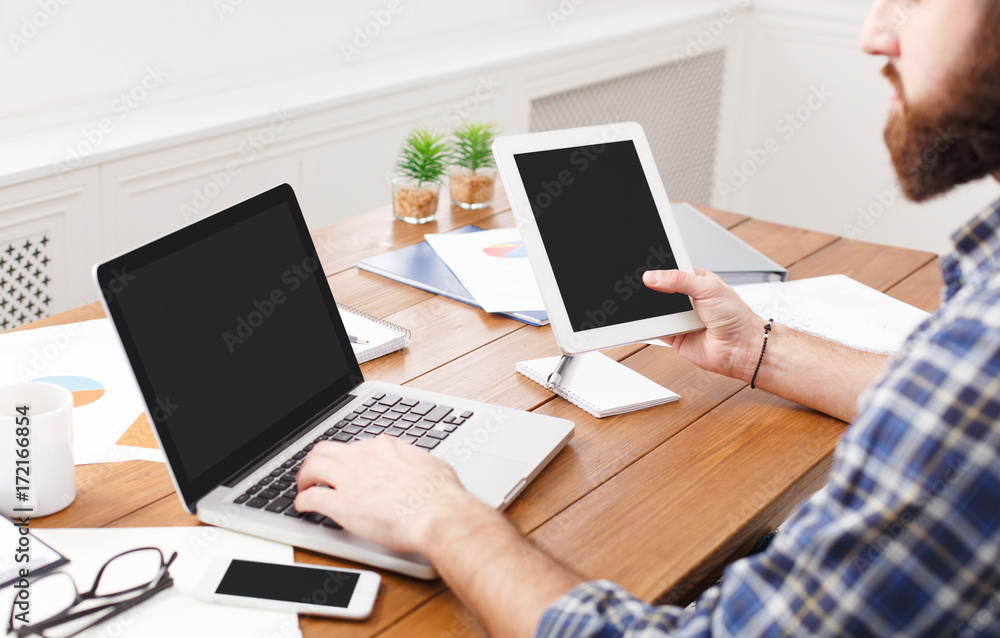 Young casual businessman working with laptop and tablet in office, close up Young casual businessman working with laptop and tablet in office, close up