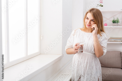 Smiling pregnant woman talking on her smartphone, copy space.