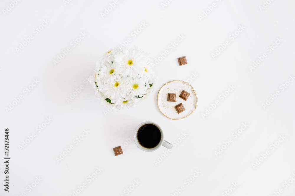 Morning breakfast with coffee cup and chocolate decorated with chamomile flowers bouquet on white background. Flat lay, top view women background.