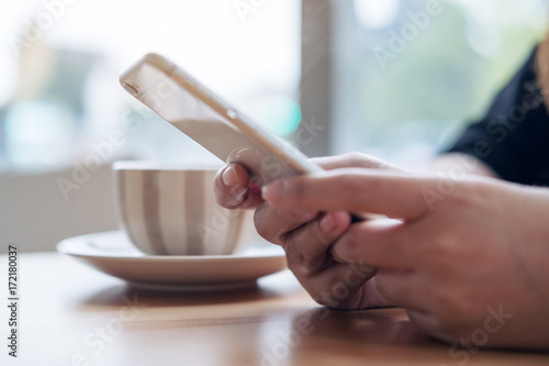 Closeup image of a woman holding and using smart phone with coffee cup on wooden table in cafe