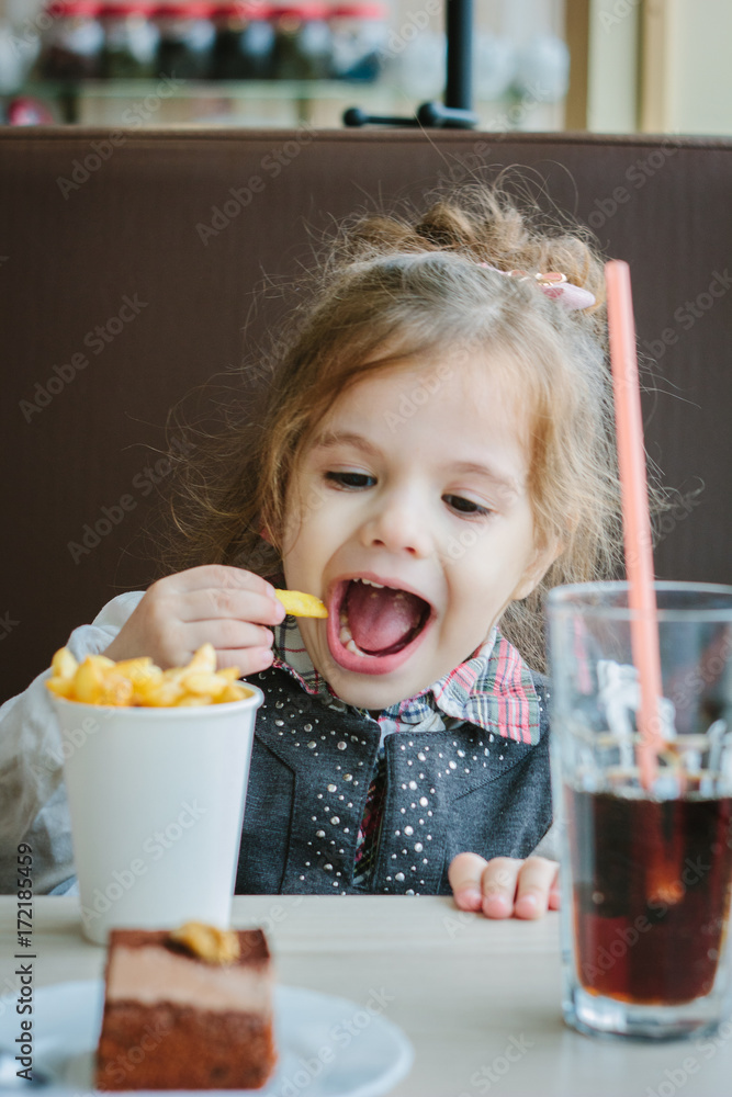 Little girl in a restaurant eating french fries and drinking cola. Little girl in a restaurant eating french fries and drinking cola.