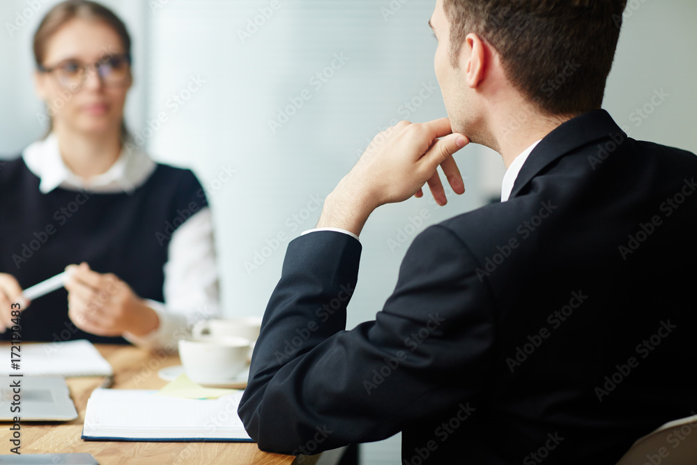 Back view of young manager gathered together with female colleague at boardroom and having productive project discussion, blurred background Back view of young manager gathered together with female colleague at boardroom and having productive project discussion, blurred background
