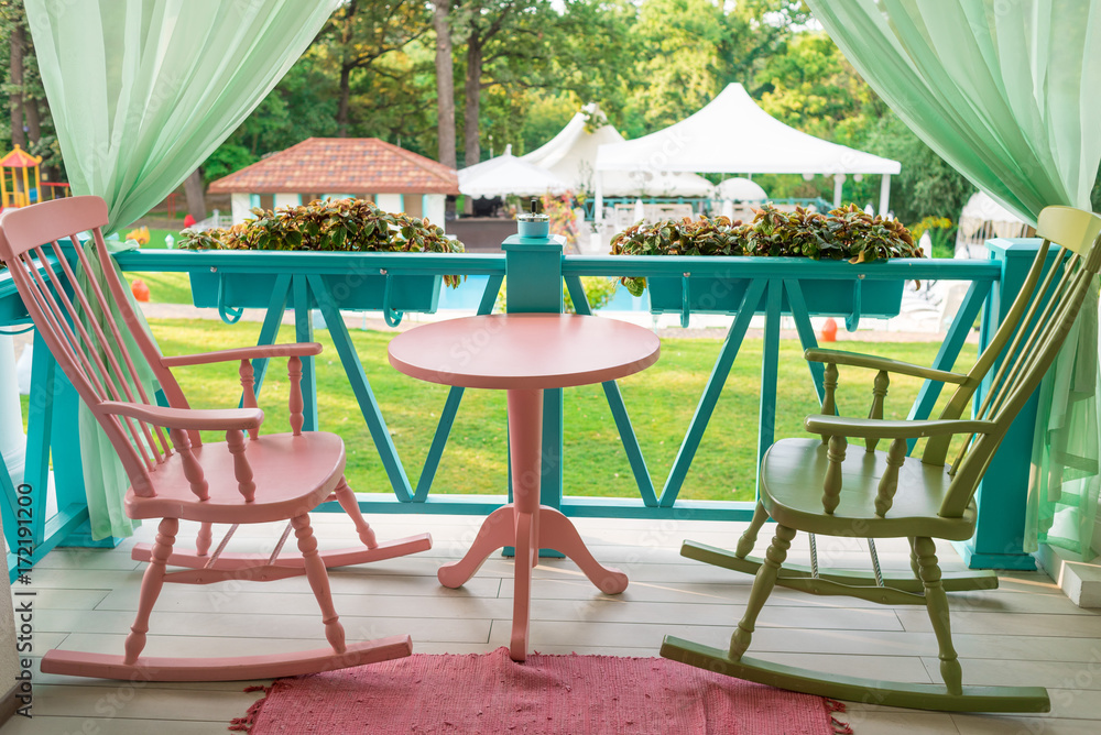 Pink and green wooden rocking chairs and table on porch or balcony. Two relaxing armchairs on porch of luxury hotel. Empty cafe with rocking chairs and table on summer  terrace outdoor, free space