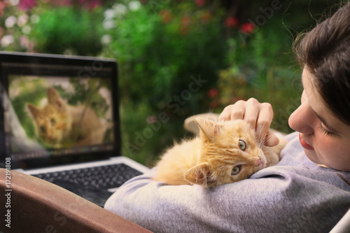 teenager girl working on retouch photo on laptop with red kitten on the green flower garden summer background photo