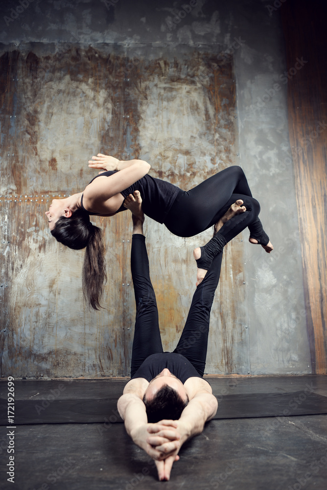 Young athletic couple practicing acroyoga. Balancing in pair. Fit active  pair yoga time. Sporty handsome man supporting and holding slim beautiful  brunette woman. Training time. Asana Stock Photo