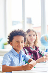 Intercultural boys sitting by desk at lesson of drawing
