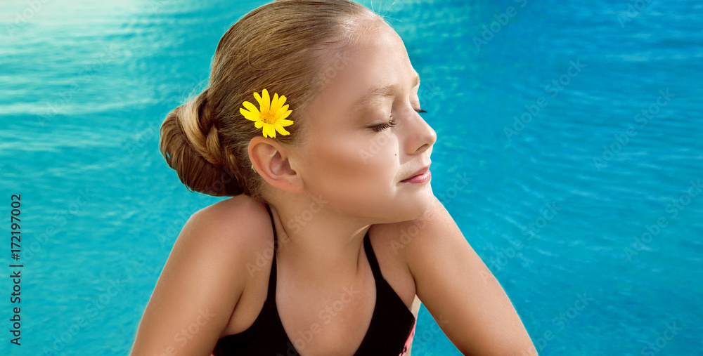 Beautiful young girl ,little princess with blonde hair with a bun hairstyle  and with a yellow flower in hair, standing in the Spa pool and looks  lovely, cute, beauty and sweet Stock