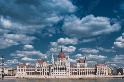  Hungarian Parliament on the embankment of Danube river against dramatic blue sky in Budapest, Hungary