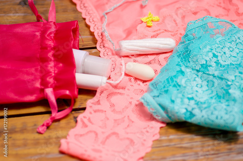 Close up of a a menstruation cotton tampon and an ovum, over a pink and blue woman underwear, and red cotton bag, in a wooden table, in a blurred background