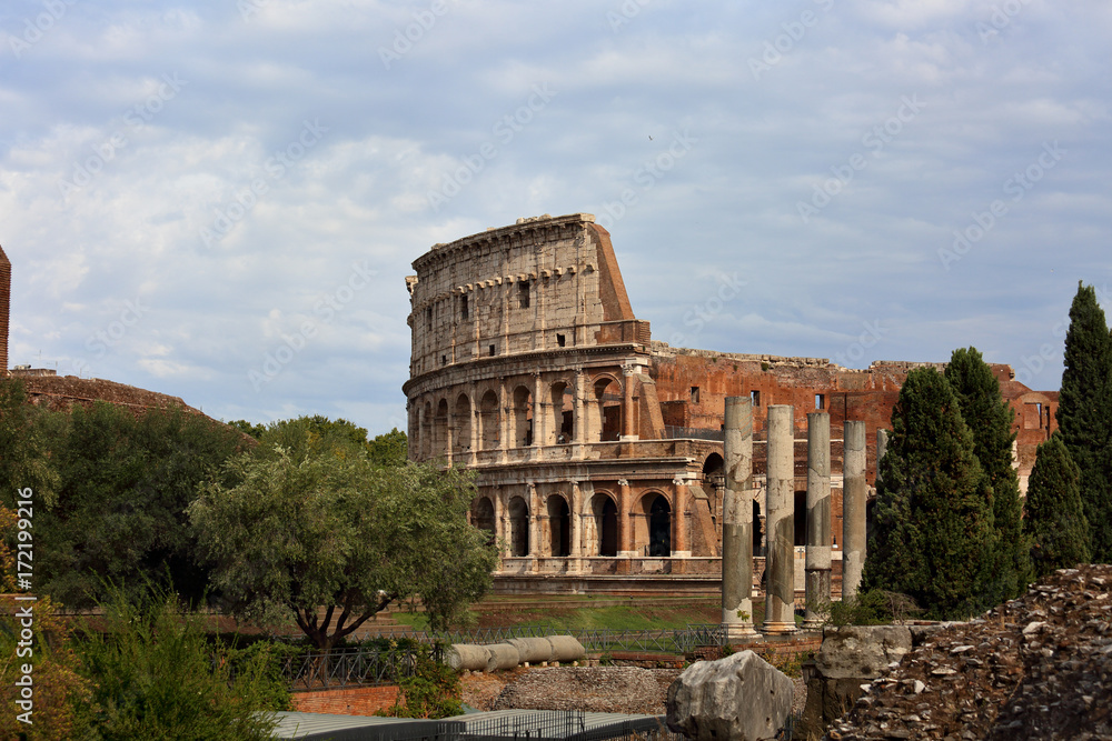 Beautiful landscape of Coliseum near the green trees under the blue summer sky. Rome