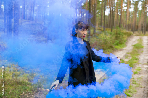 Young woman in forest having fun with blue smoke grenade  bomb