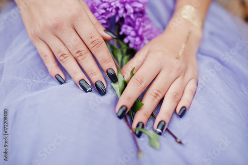 Violet aster flowers at hands with black manicure of girl.