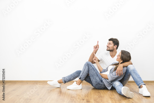 The happy couple sit and gesture on the background of the white wall