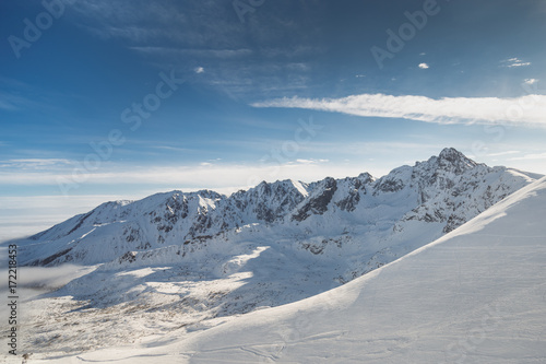 Wide shot aerial view of snow capped cold rock mountains with sunny blue skies