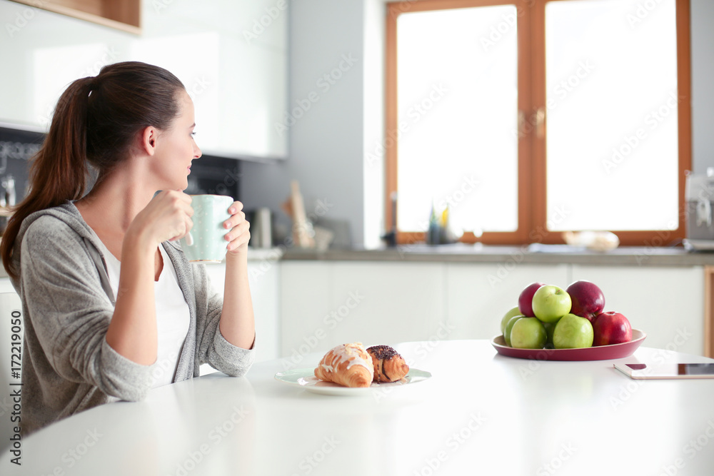 Woman drinking tea with sweet croissant at the kitchen table.