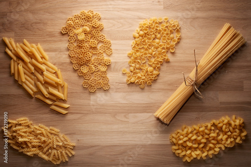 Several types of dry pasta on light wooden table
