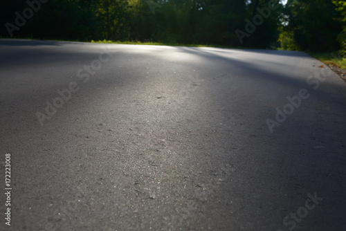 Asphalt road passing through the forest. Asphalt coating background texture. New fresh asphalt. Lights and shadows