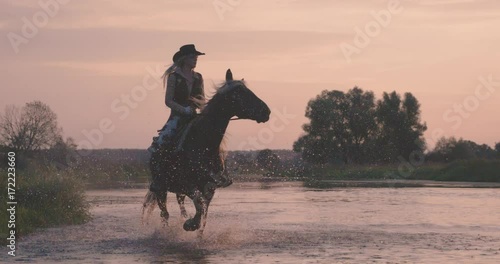 Slow motion 240fps shot of cowboy girl riding horse in water of sunset river