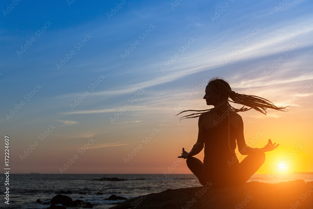 Yoga woman silhouette on the sea beach during sunset.