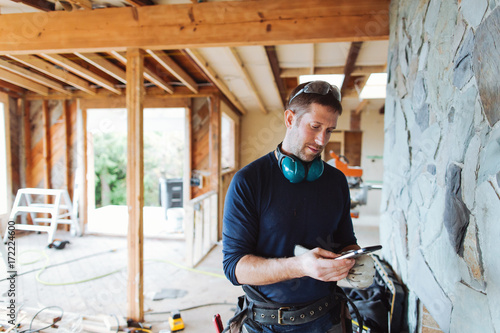 Carpenter contractor texting on cell phone inside home renovation photo