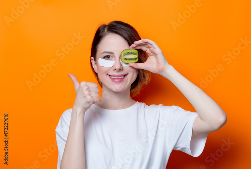 Woman using eye patch for her eyes and holding kiwi