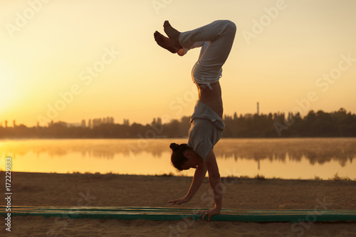Young athletic men standing in yoga pose on near lake in the par