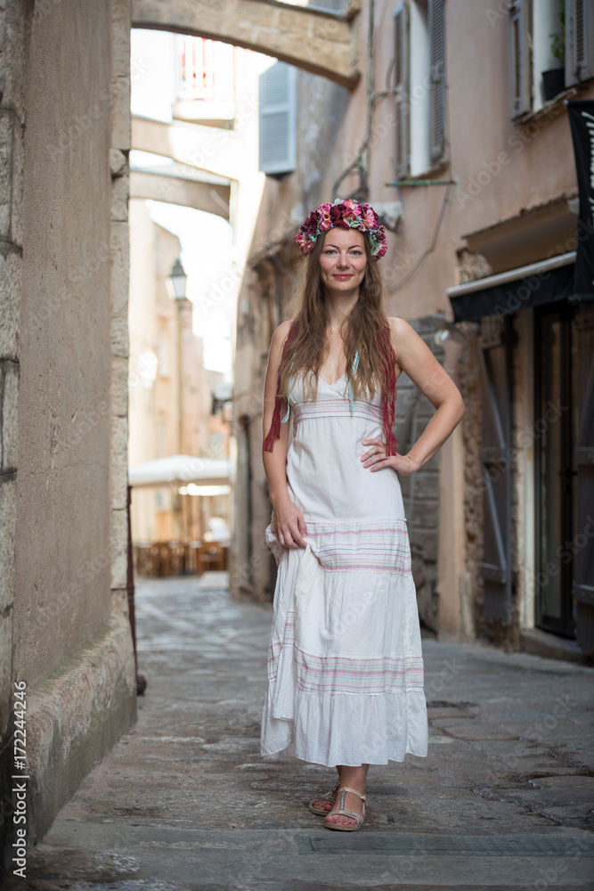 Young woman in white dress with flower head band in streets of Bonifacio, France