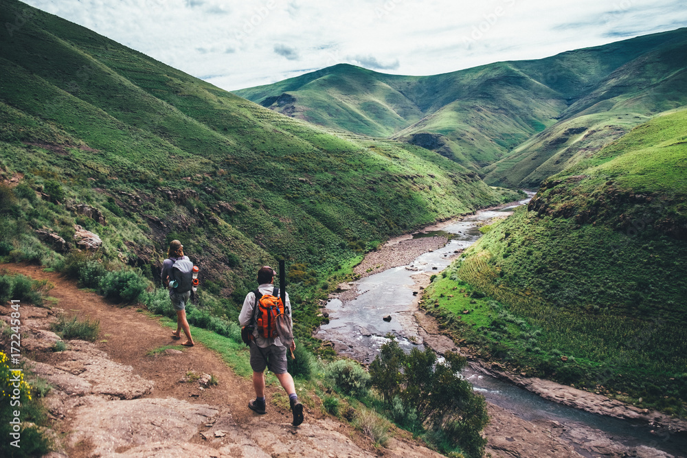 fly fishermen hikers walking on a mountain path overlooking a valley and river fly fishermen hikers walking on a mountain path overlooking a valley and river