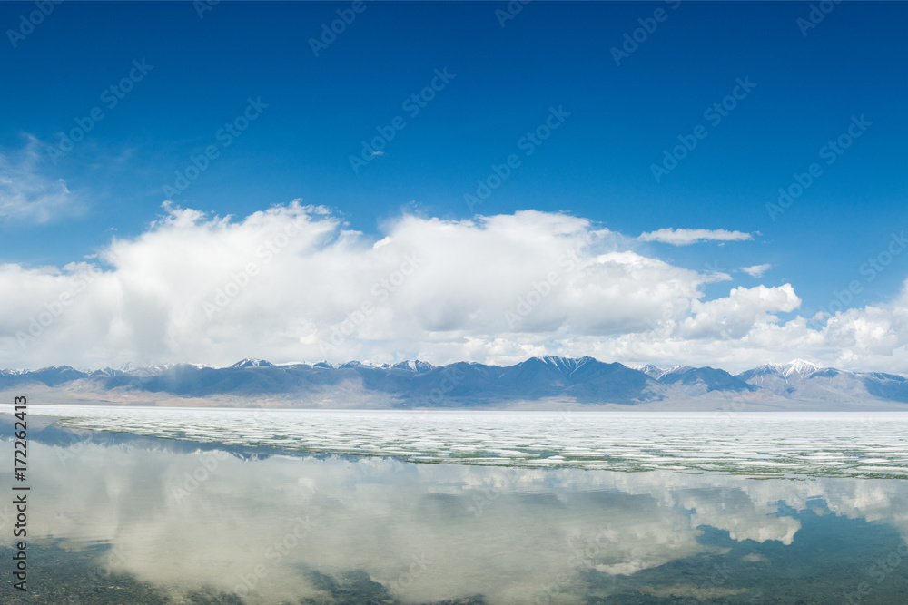 panoramic view of fluffy white clouds reflecting in mirror water of lake
