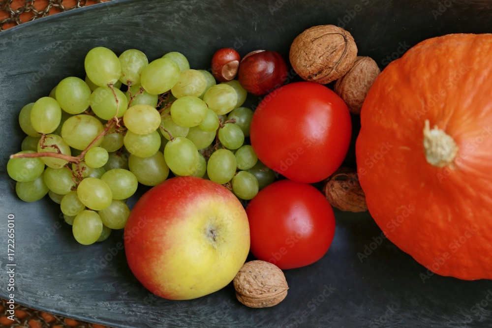 Fruit bowl with red tomatoes, apple, nuts, grapes and pumpkin