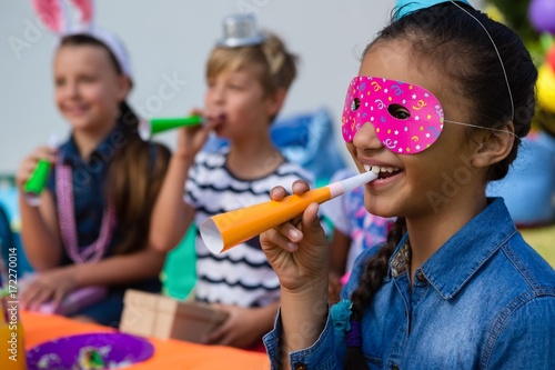 Close up of girl wearing eye mask blowing party horn