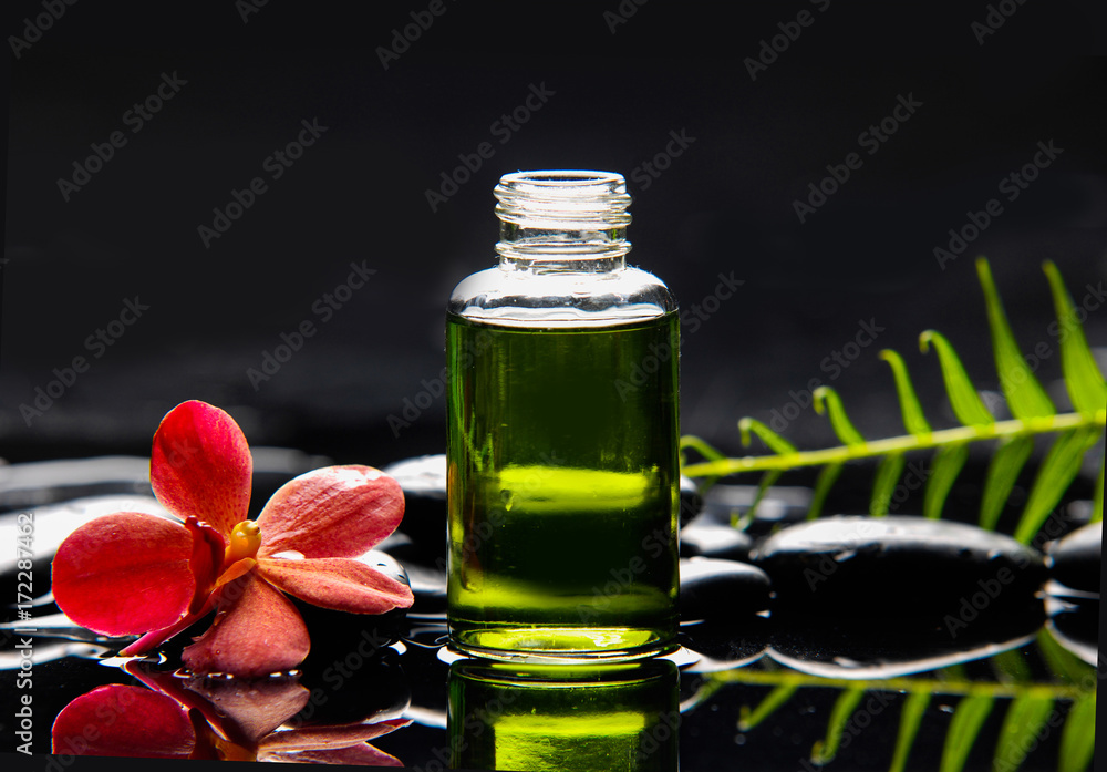 Single red orchid with fern and stones ,oil in glass on wet background Single red orchid with fern and stones ,oil in glass on wet background